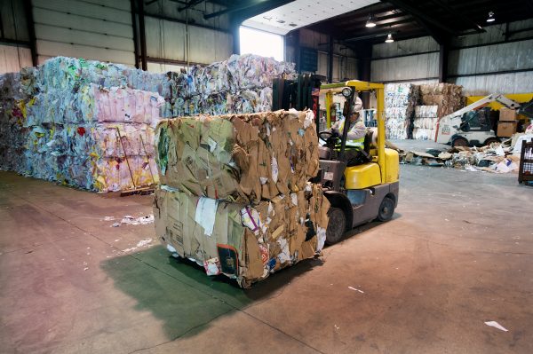 Baled recyclables being transported by an equipment operator processor where it will be stored until it's picked up by a processor.